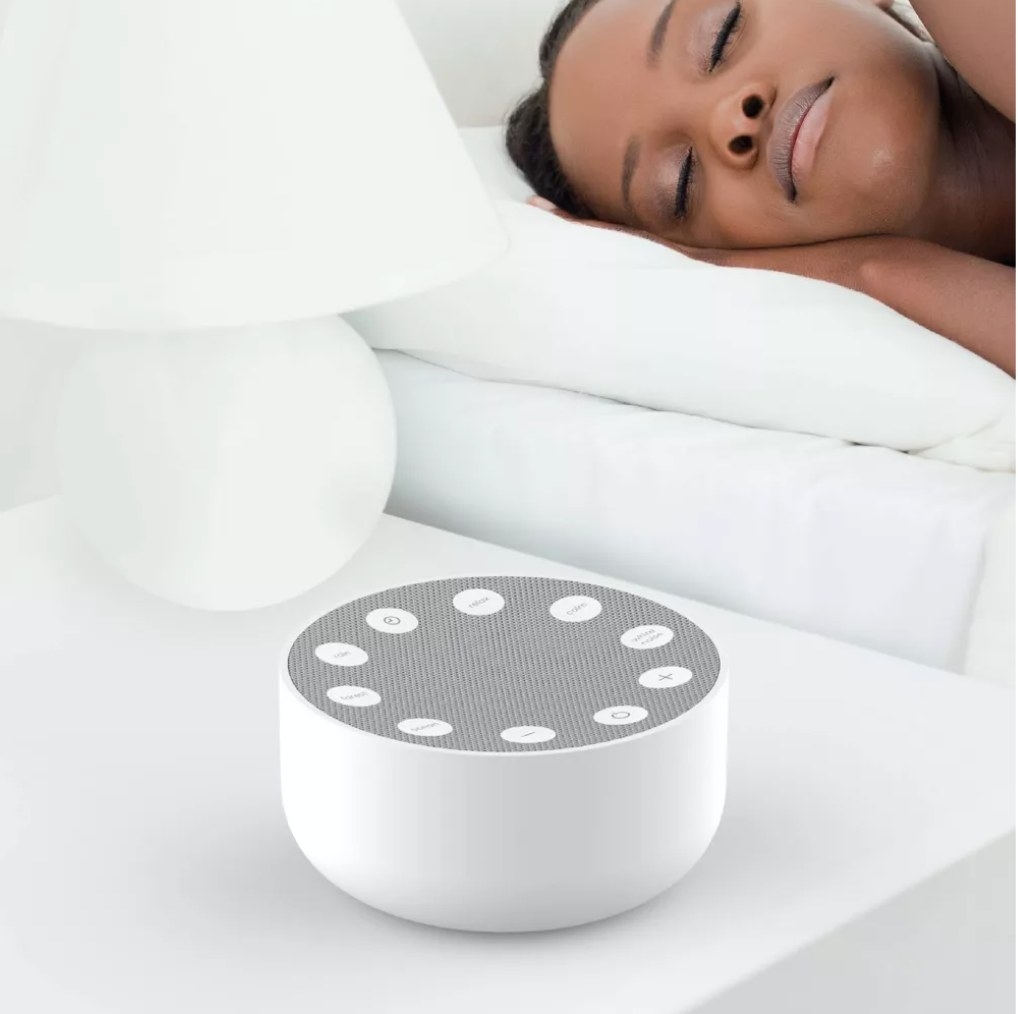 a model sleeping next to the white and grey sound machine