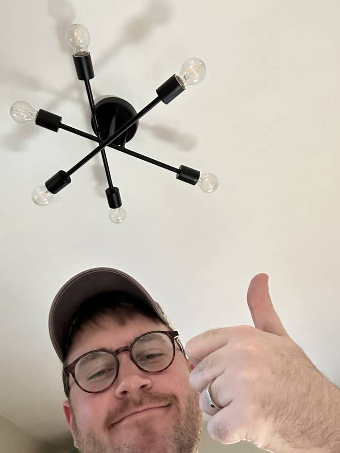 author giving sarcastic thumbs up under mid-century modern light fixture that he hates