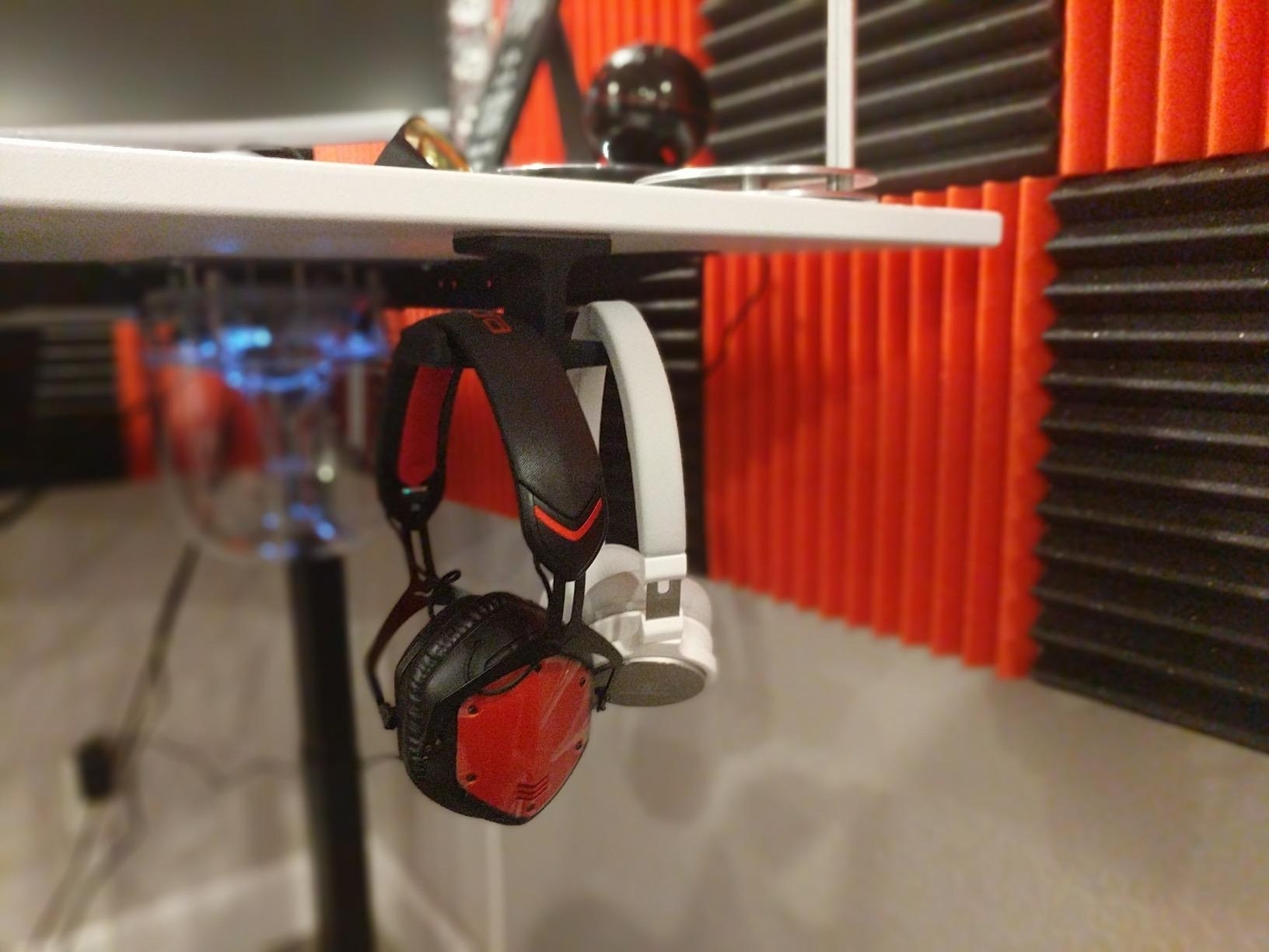 a reviewer photo of two pairs of headphones hanging under a desk
