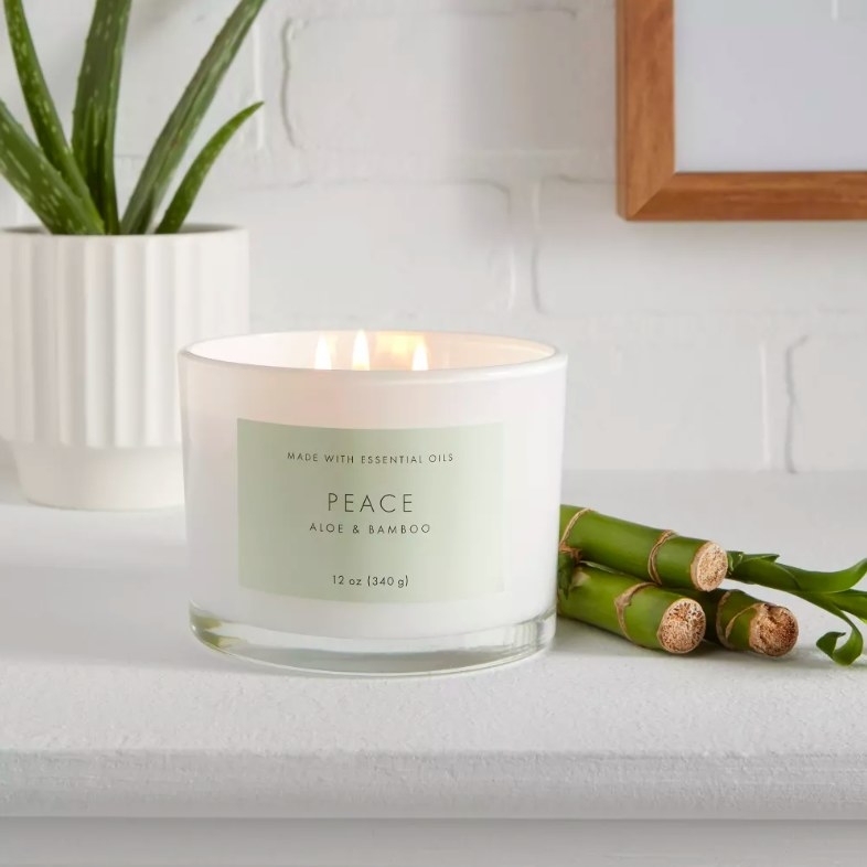 Lit candle in a white container next to green bamboo