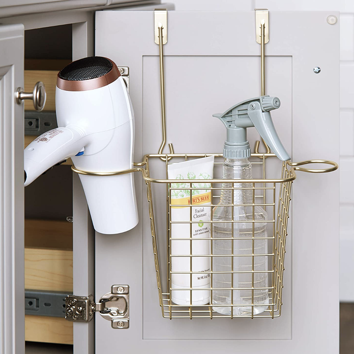 open bathroom cabinet door with basket-like over-the-door hanging organizer in gold filled with hair tools