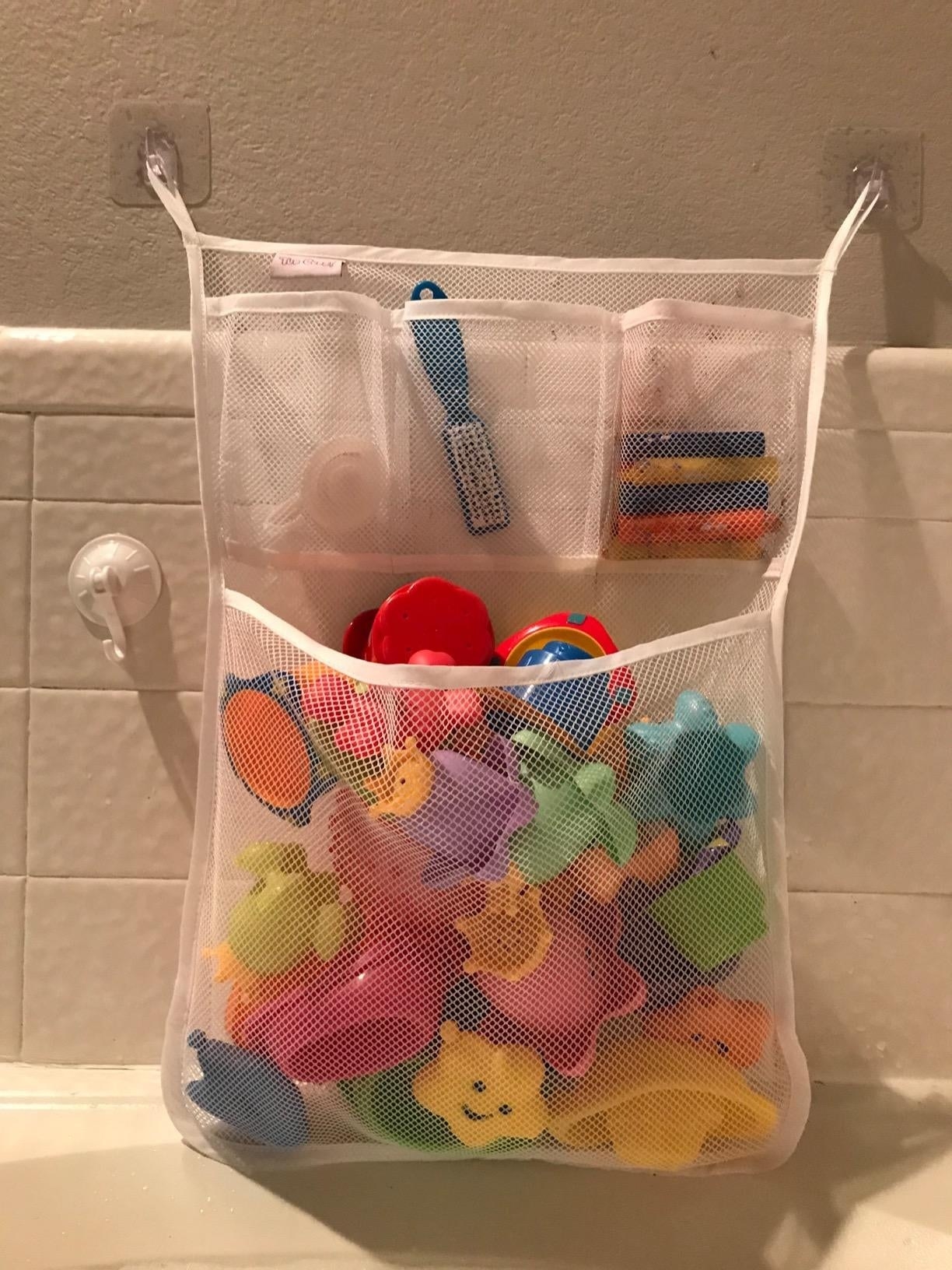 reviewer&#x27;s photo of a mesh organizer containing bath toys and stuck to the wall