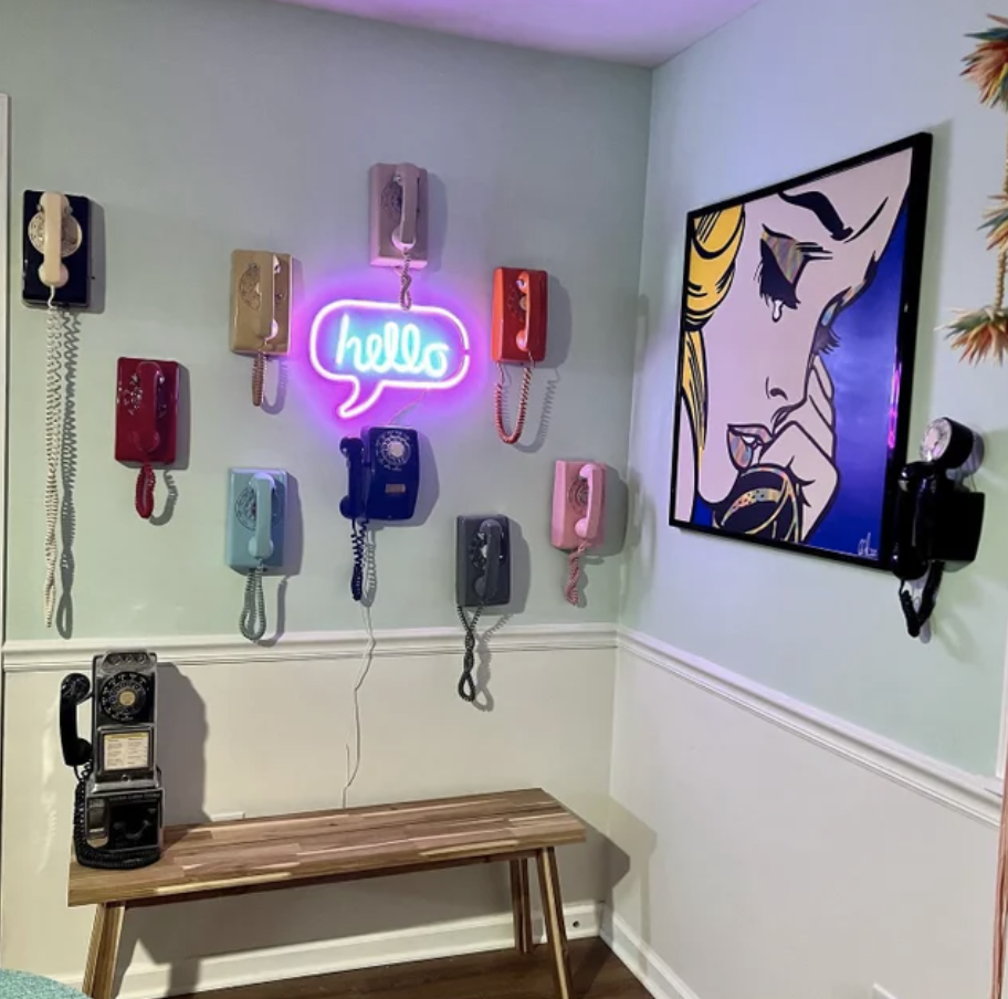 A collection of corded rotary phones in different colors hanging on a wall