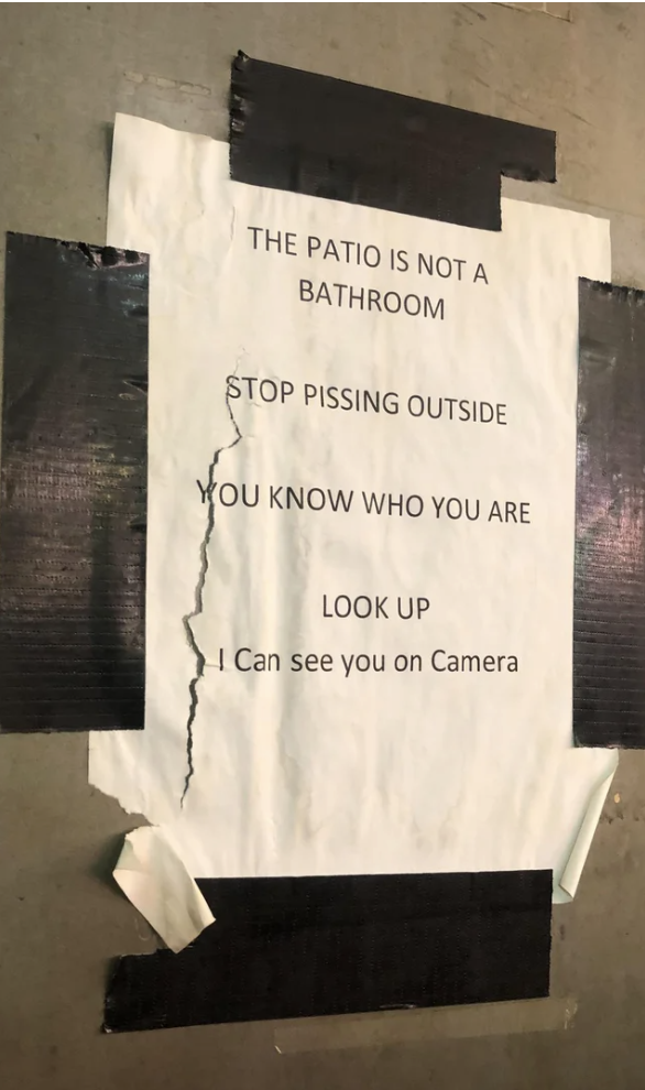 The sign says &quot;the patio is not a bathroom, stop pissing outside, you know who you are, look up, I can see you on camera&quot;