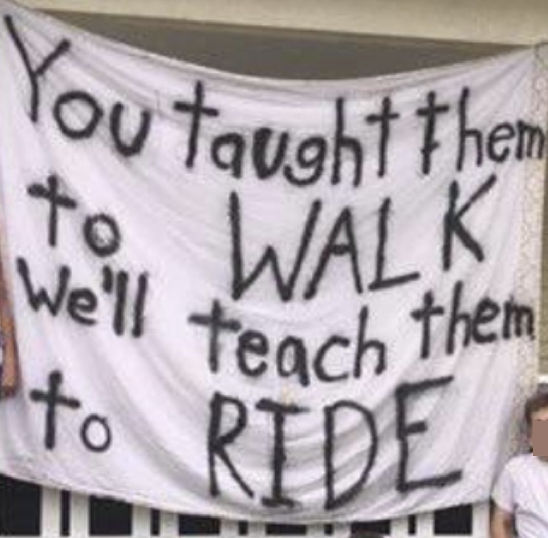 Members of a fraternity on the front lawn with a huge sign that says &quot;you taught them to walk, we&#x27;ll teach them to ride&quot;