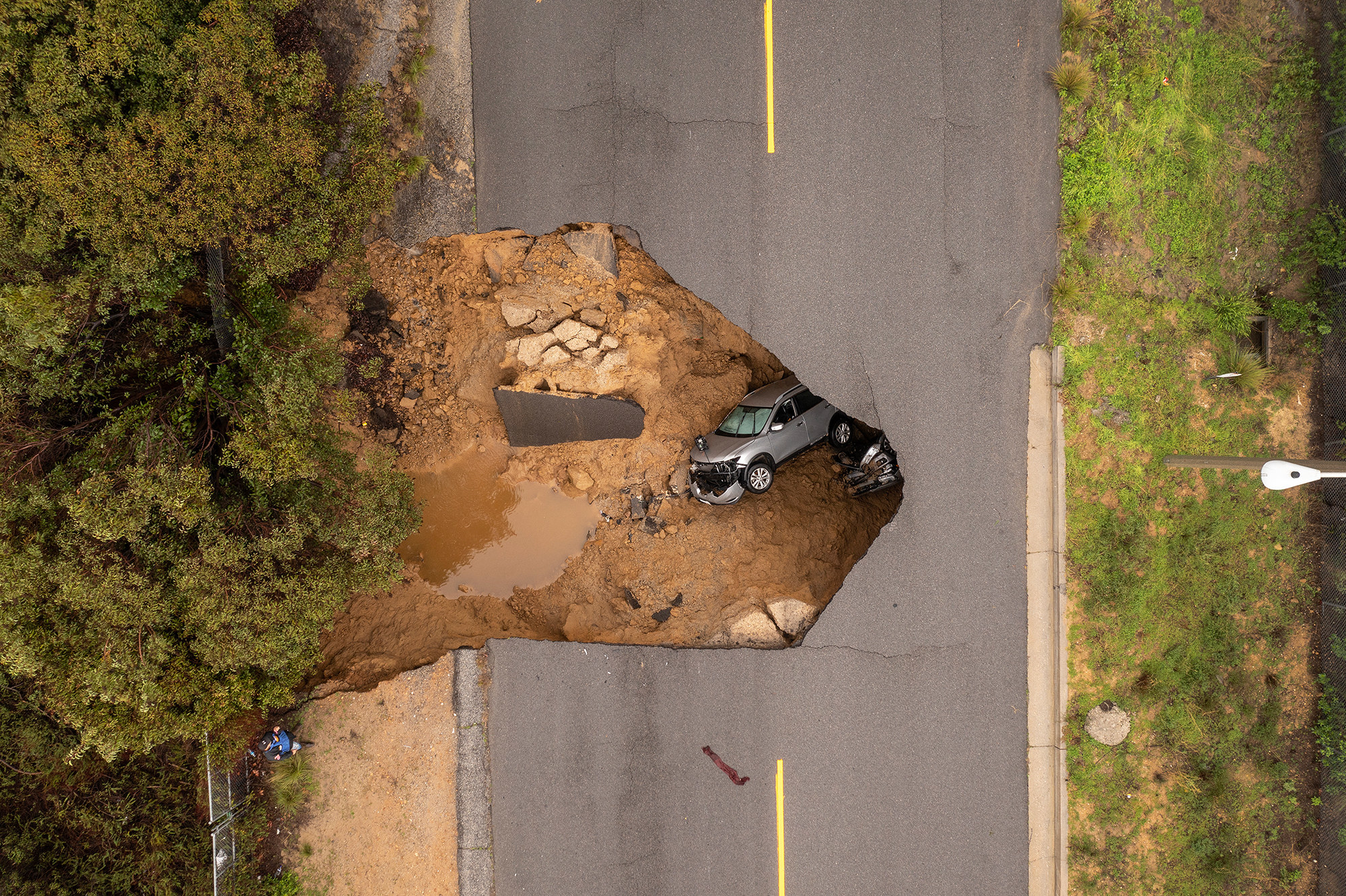 Aerial shot of a sinkhole on an open road. Inside the sinkhole are a car and a pickup truck