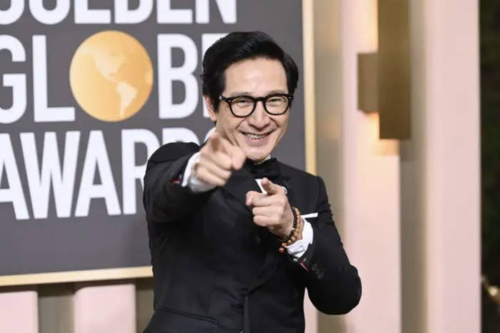 Ke Huy Quan looking like a king in a suit and black glasses and smile. He's pointing at the camera and slaying