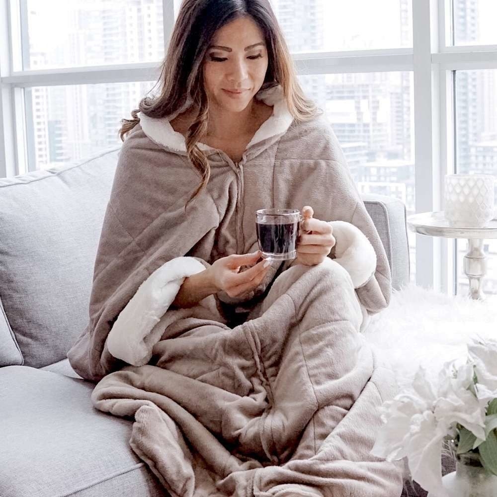 person wrapped up in the zipped blanket with a mug