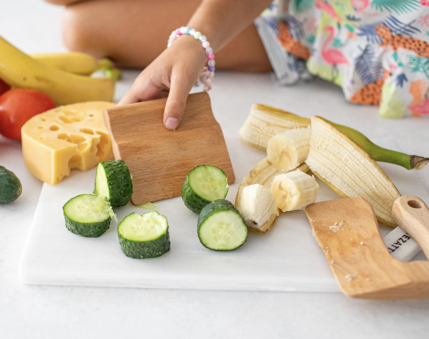 A child holding the wooden knife with chop fruits and veggies around