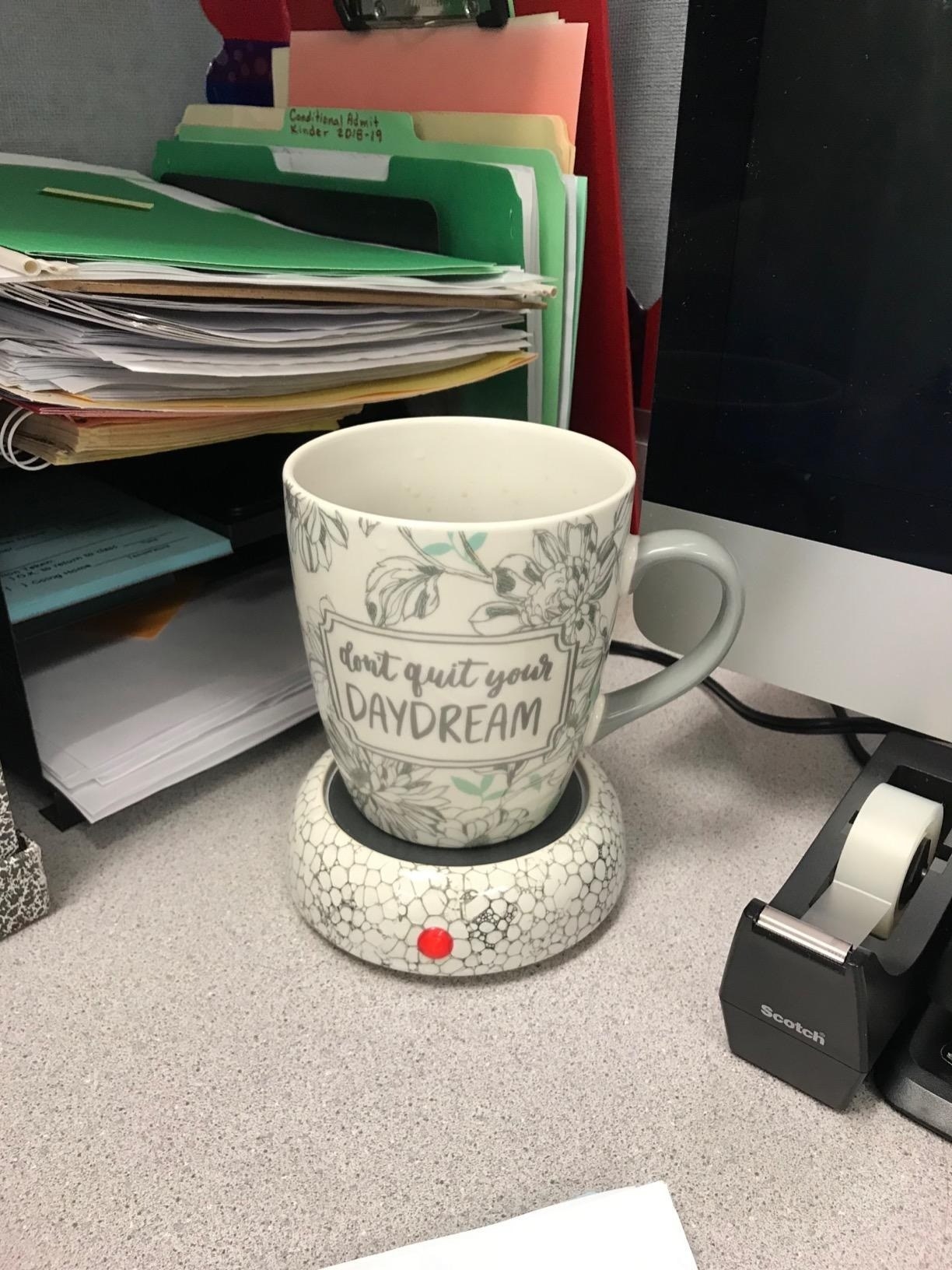 reviewer image of a mug sitting atop the mug warmer which sits on a desk