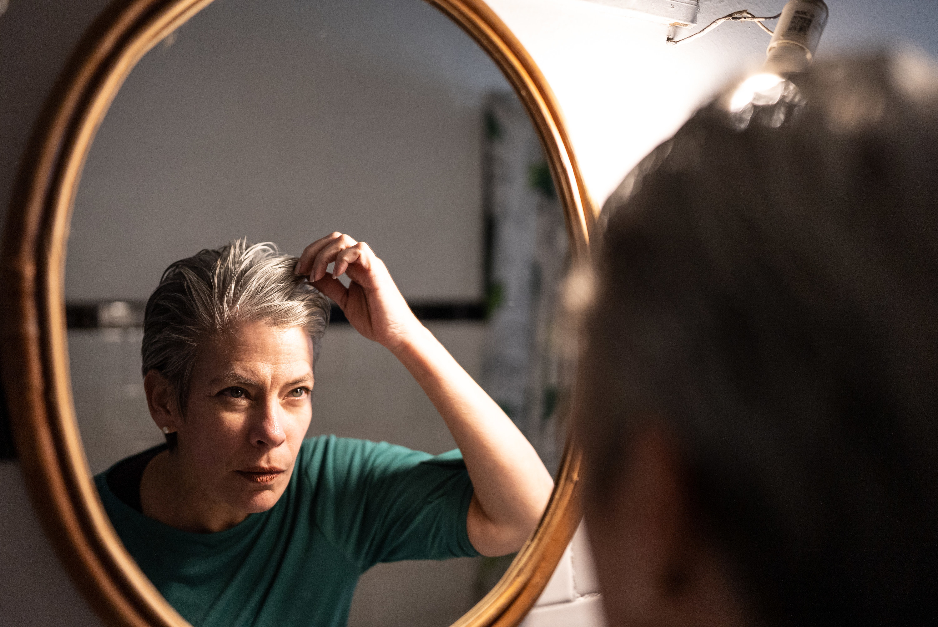 a woman checking her grey hair in the mirror