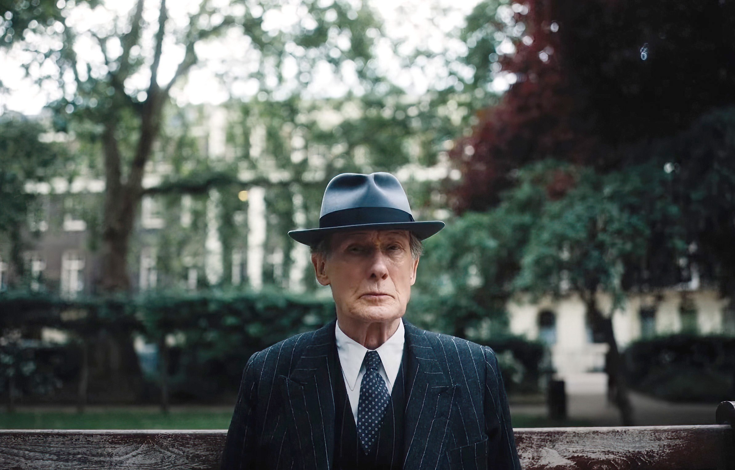Bill Nighy stands in the street with a hat on