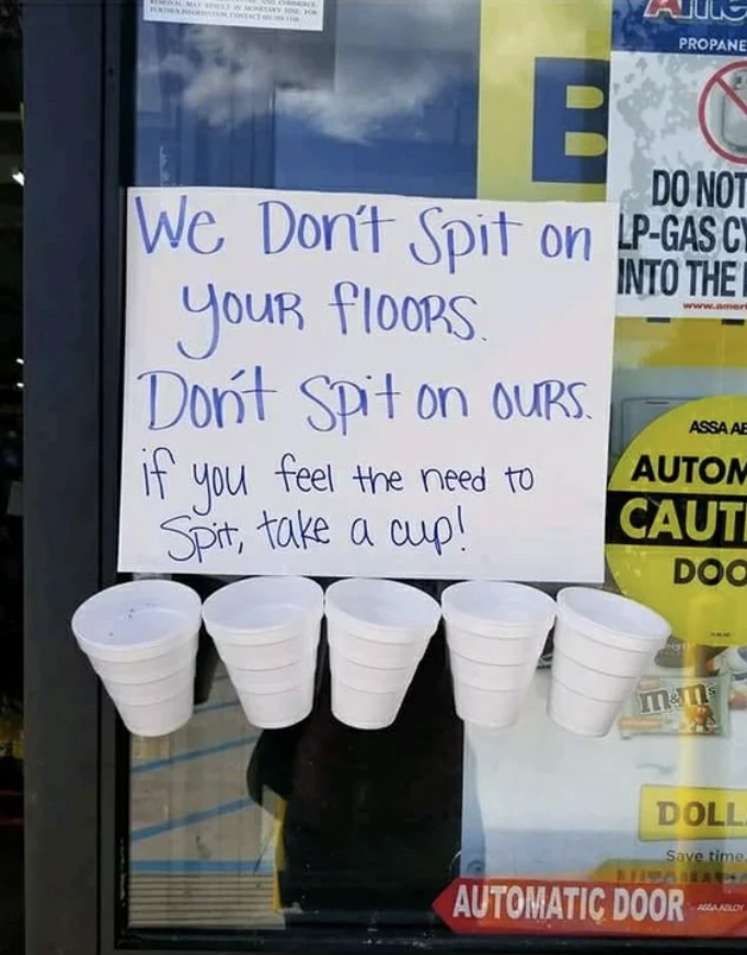 The sign says &quot;We don&#x27;t spit on your floors, don&#x27;t spit on ours; if you feel the need to spit, take a cup&quot; with a row of five cups taped to the bottom of the sign