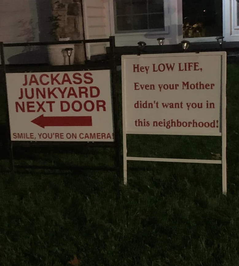 Two signs next to each other, one reads &quot;jackass junkyard next door,&quot; and the other reads &quot;hey lowlife, even your mother didn&#x27;t want you in this neighborhood&quot;