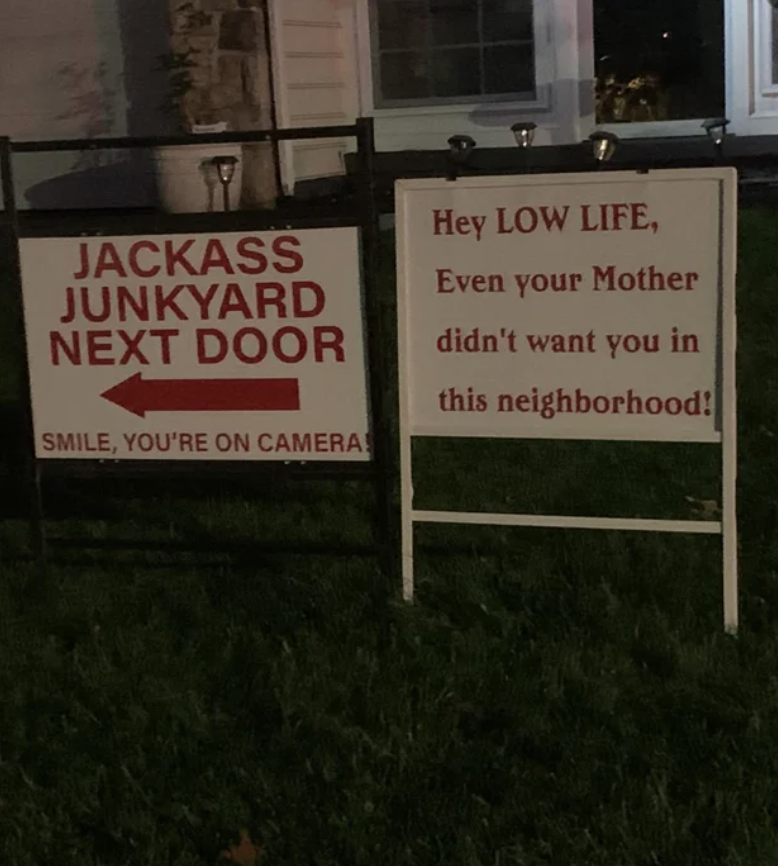 Two signs next to each other, one reads "jackass junkyard next door," and the other reads "hey lowlife, even your mother didn't want you in this neighborhood"