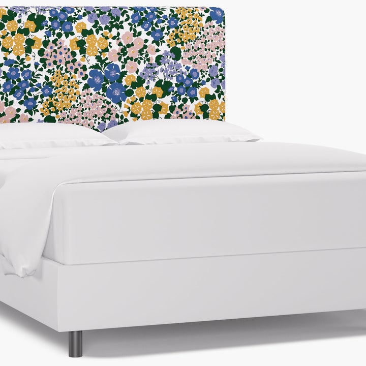 A bed with a yellow, purple, pink, and blue floral headboard