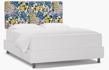 A bed with a yellow, purple, pink, and blue floral headboard