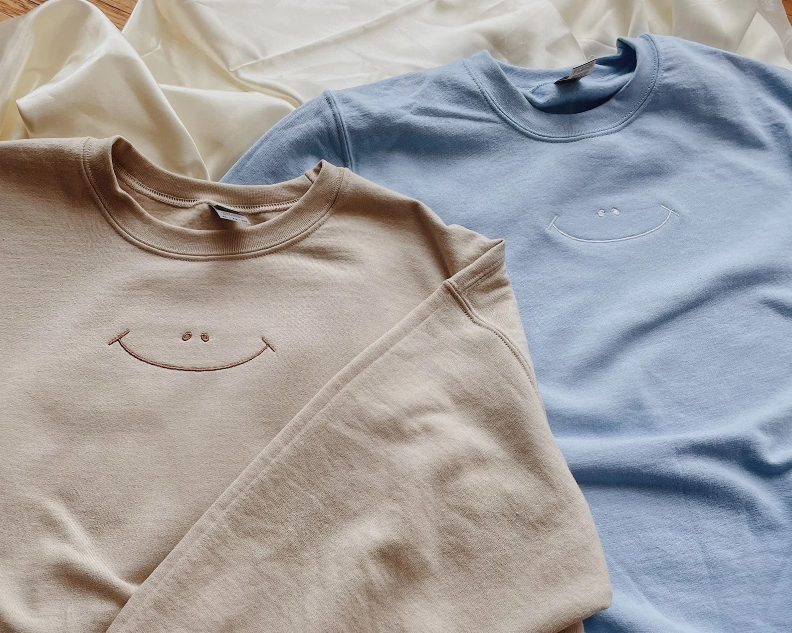 Beige and blue crewnecks with smiley faced embroidered on upper center