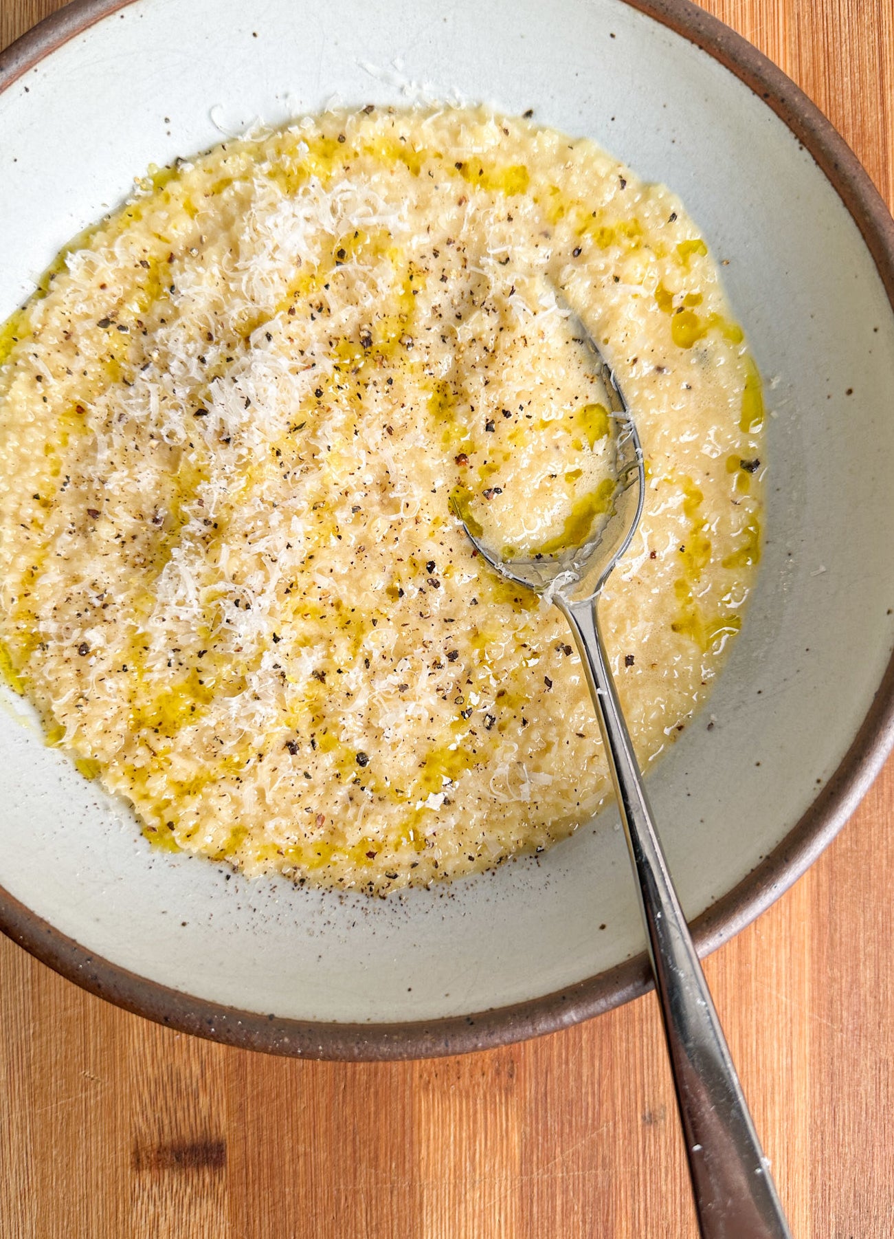 pastina in a white bowl with spoon and extra parmesan cheese, pepper, and olive oil