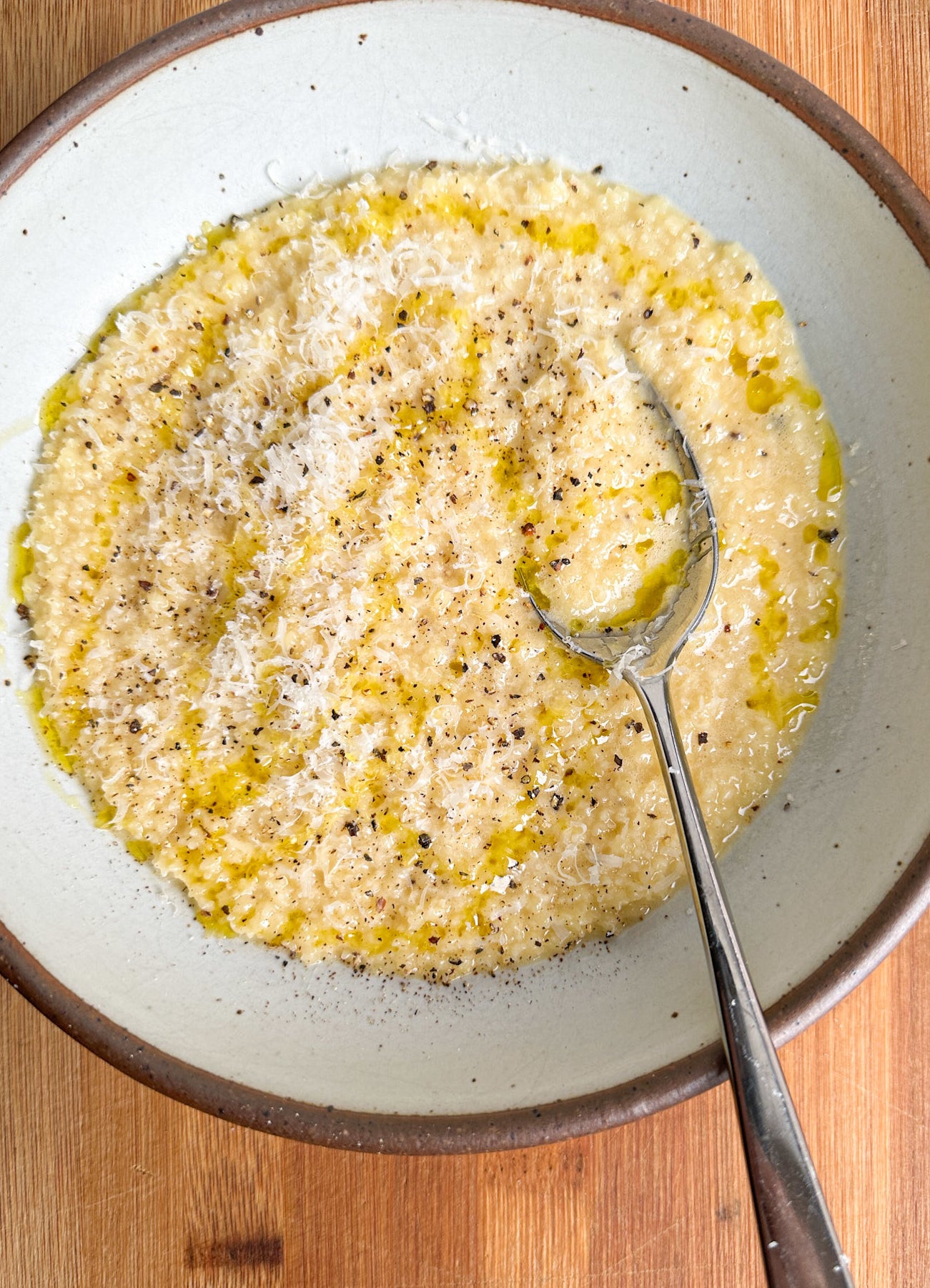 pastina in a white bowl with spoon and extra parmesan cheese, pepper, and olive oil