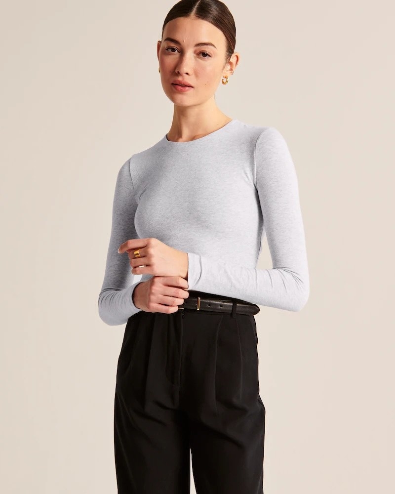 Model wearing seamless long sleeve tee in light gray with black slacks
