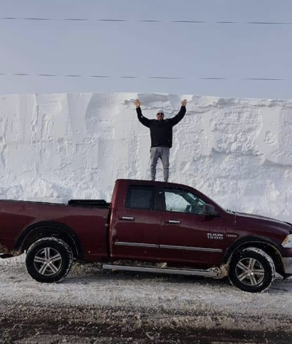 A man standing on top of his truck in front of a wall of snow
