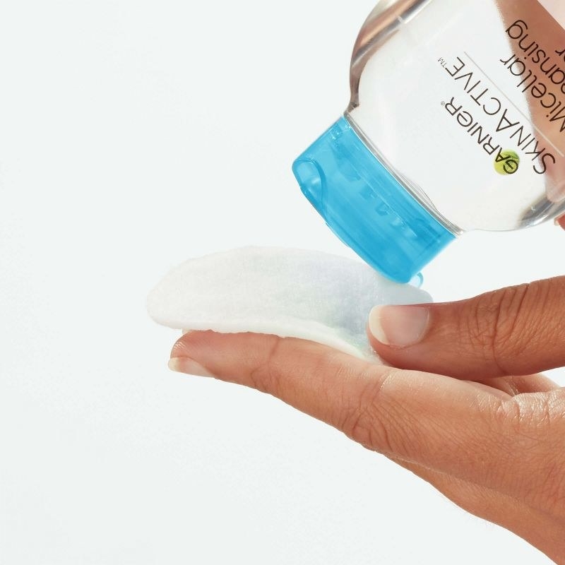 A person pouring micellar water onto a cotton round