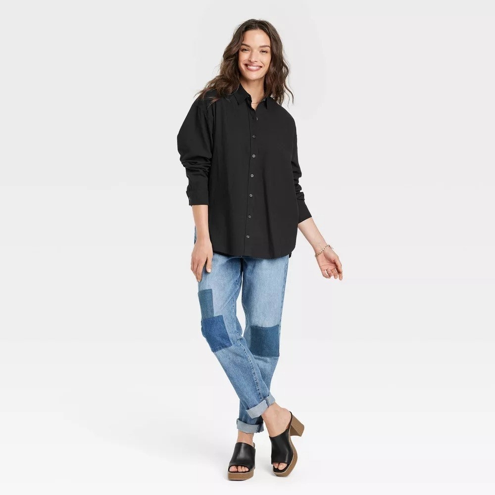 A model wearing the black button down with pieced blue jeans and black mules