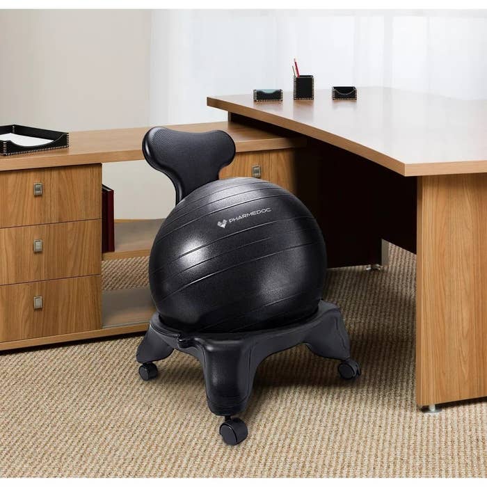 The black exercise ball with back support beside a wooden desk