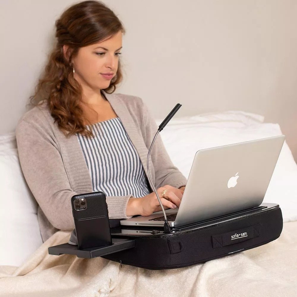 A model using the lap desk in bed with a laptop and smartphone.