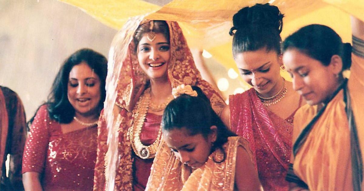A bride smiles and poses for a picture while her bridesmaids assist her