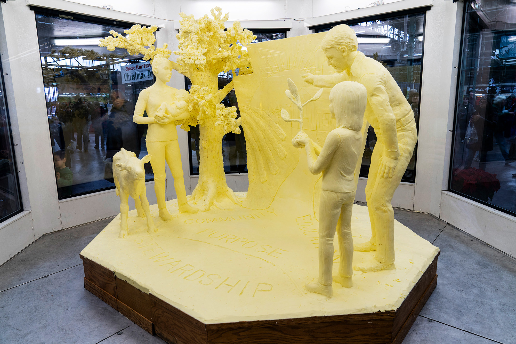 A life-size scene of people standing next to a tree and a goat composed entirely of butter