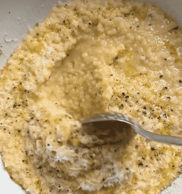creamy pastina dish with cheese and pepper getting mixed around in a bowl