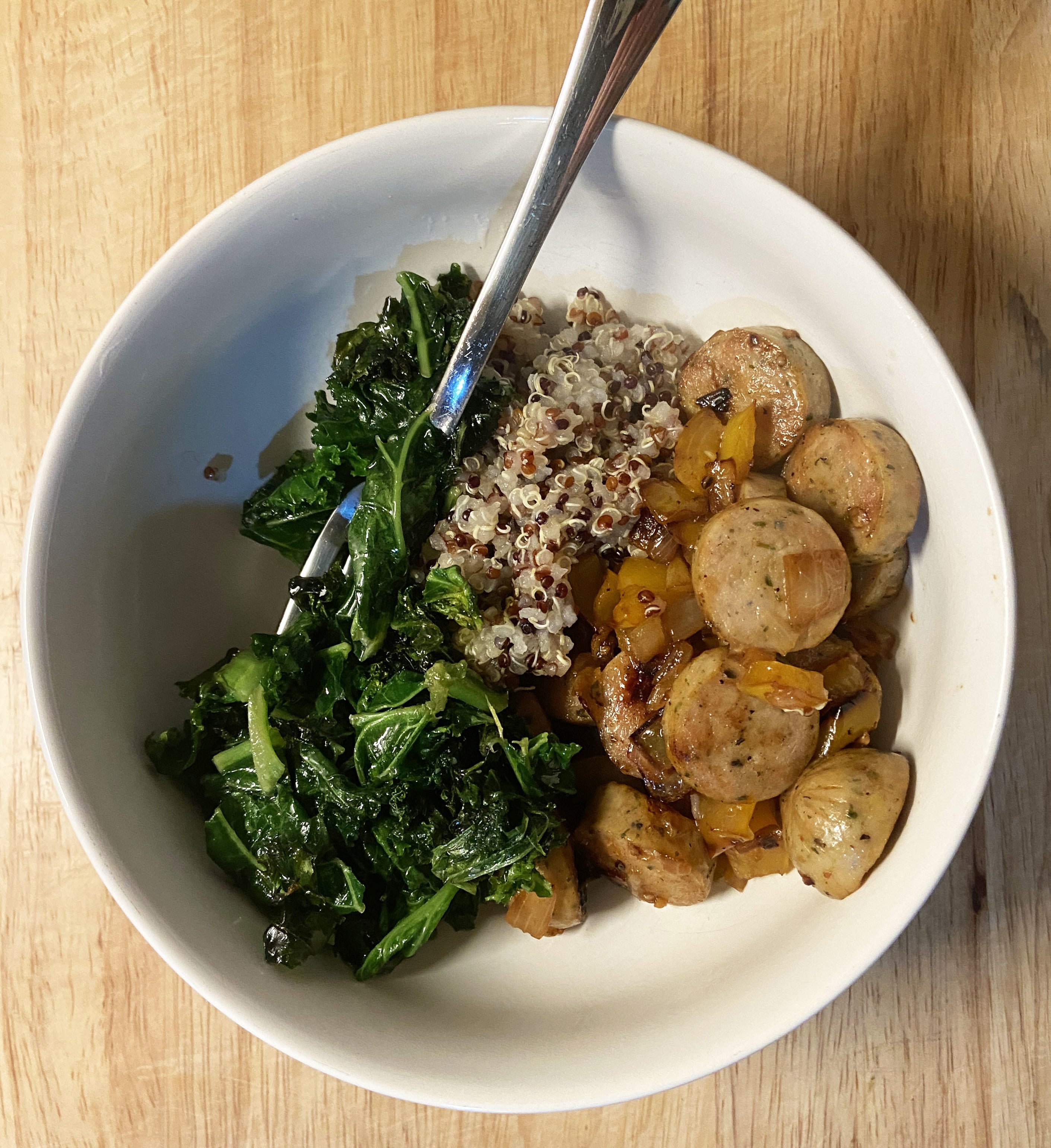 A bowl of chicken sausage, quinoa, pepper, onion, and sautéed kale