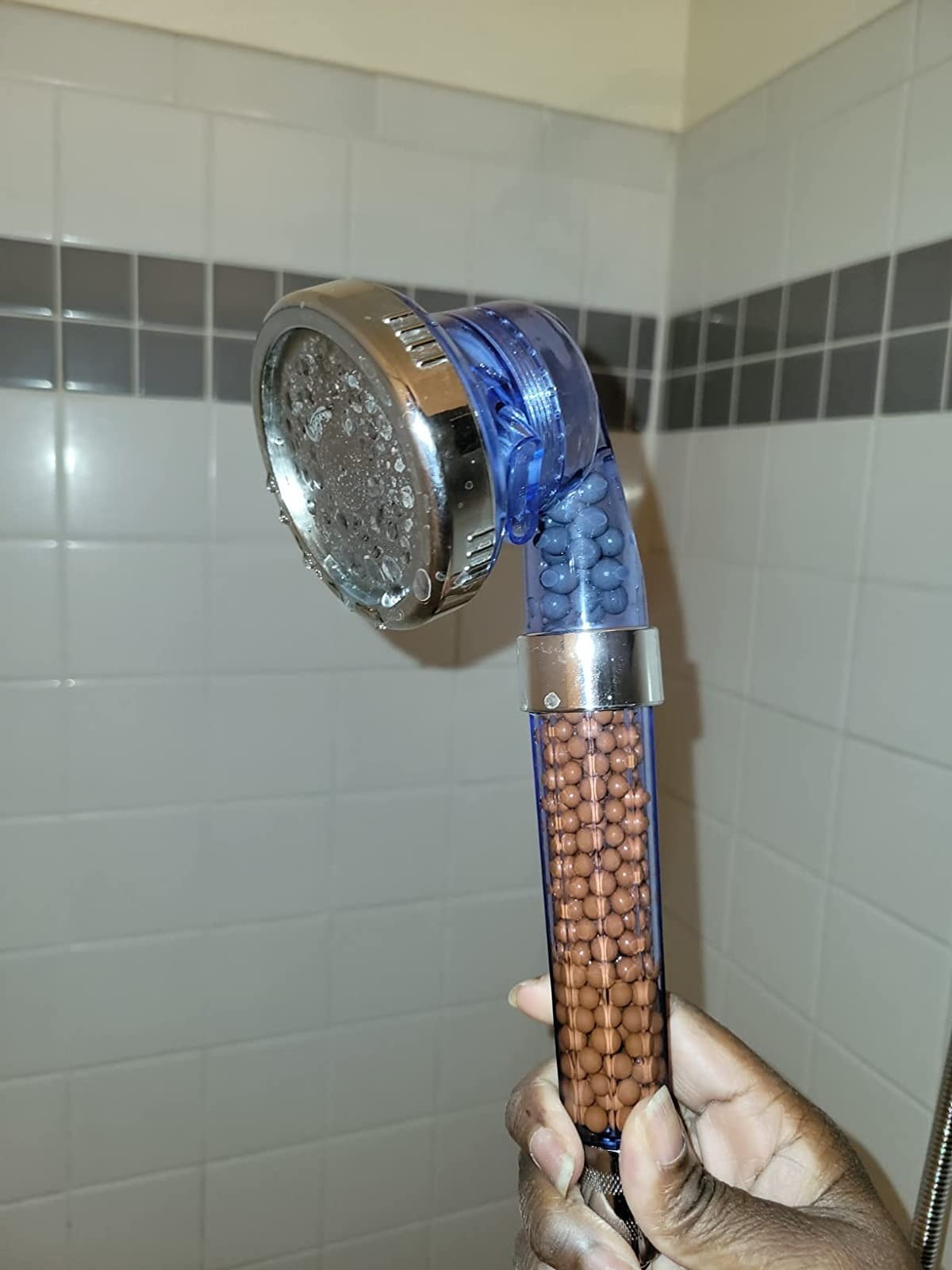 reviewer holding the clear shower head with brown filtered beads inside
