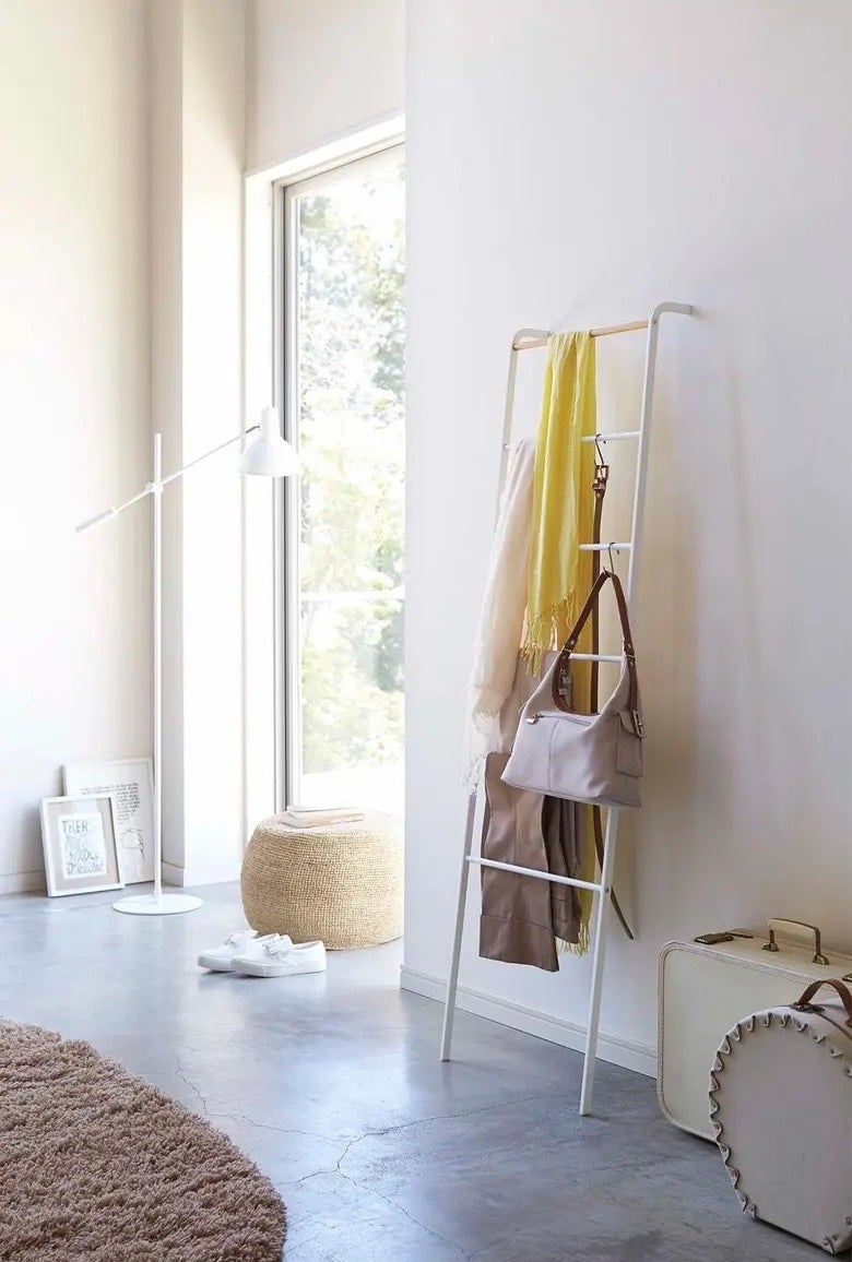 A white ladder in a home with yellow and white scarves, tan pant and a white bag