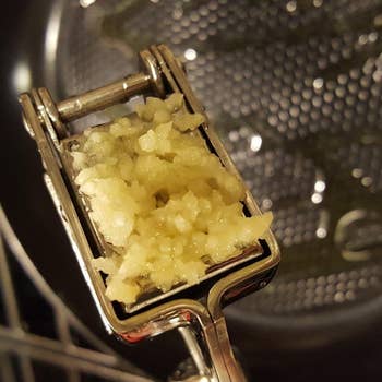 A handheld garlic press producing a thick paste of garlic