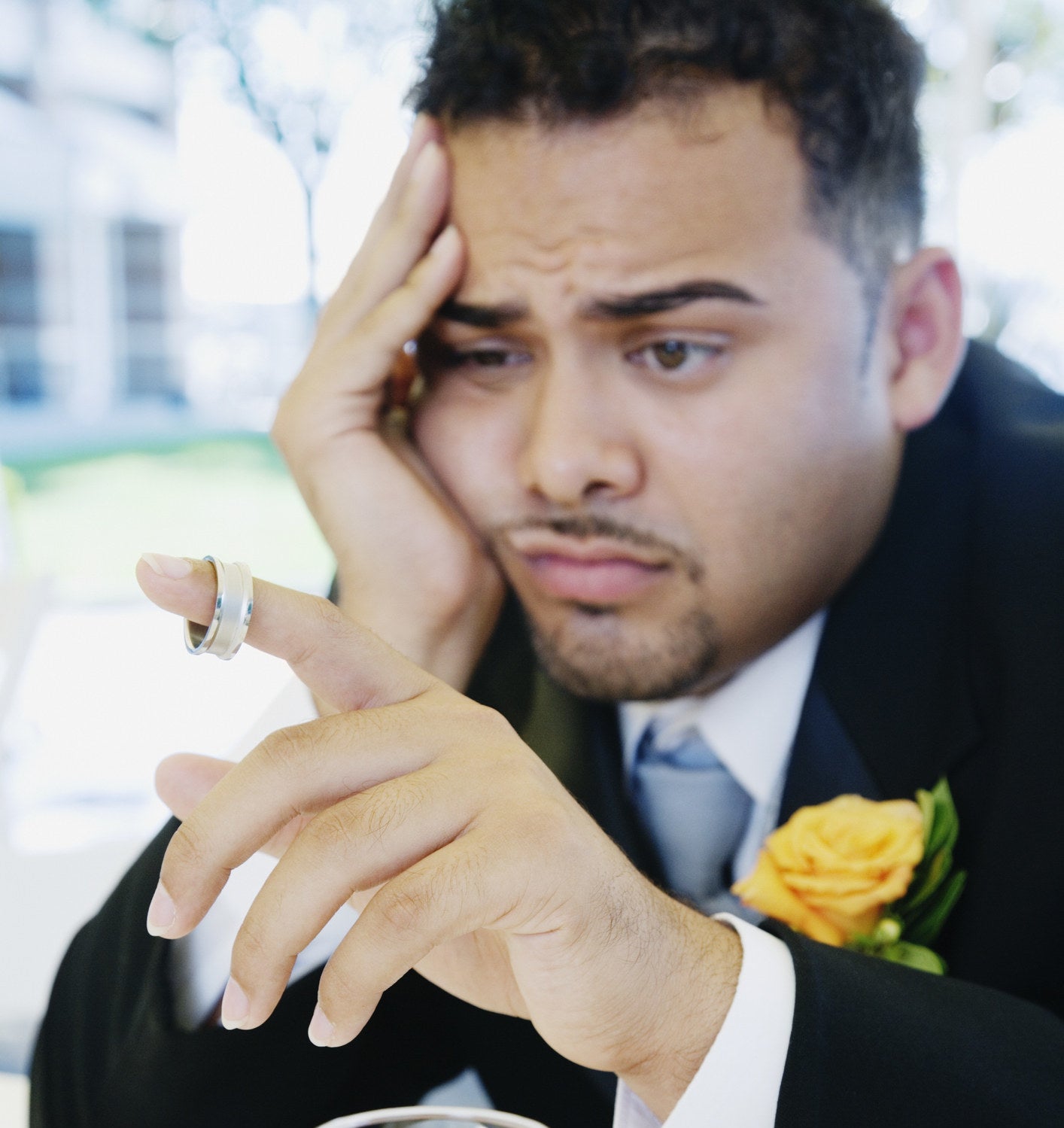 Upset-looking man wearing a suit and corsage sits with his hand holding his face