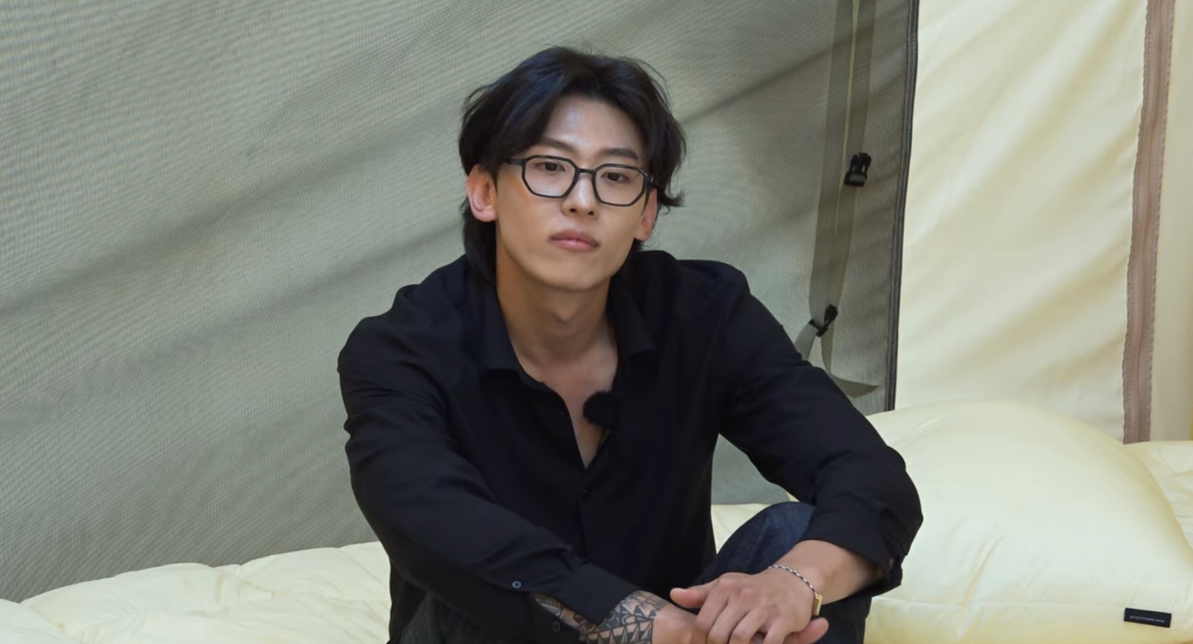 Wearing all black, Kim Jin-young sits on a bed and looks serious