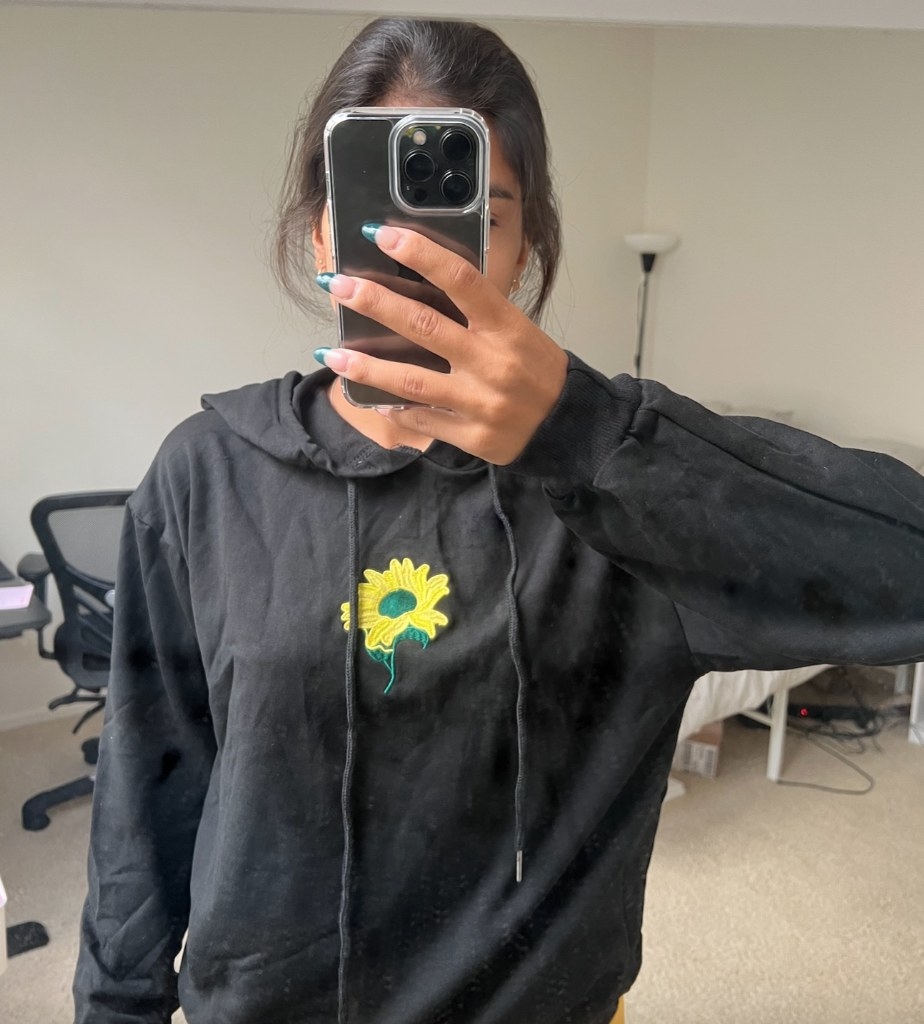 Reviewer wearing black hoodie with yellow and green embroidered sunflower in center