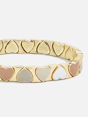 a gold bracelet with neutral colored enamel hearts around it