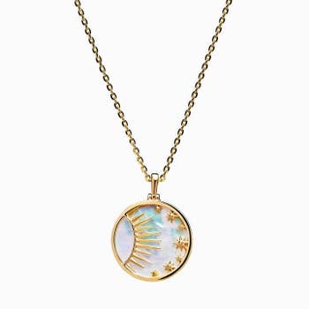 a gold circle necklace with a mother of pearl background and a sun and moon raised inside it