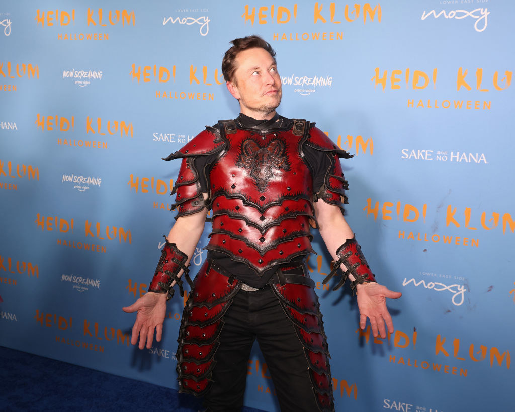 Elon Musk wearing a red medieval soldier sort of costume? There are thigh and wrist guards? He&#x27;s also doing the yoga mountain pose