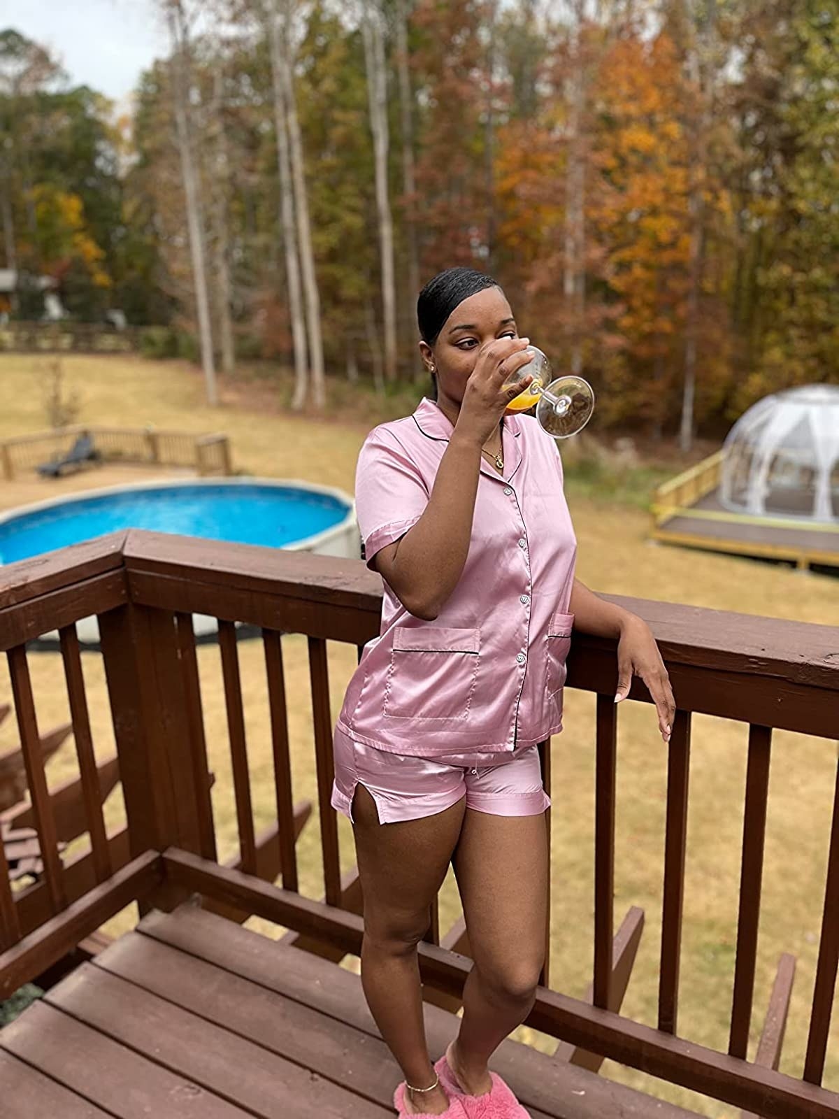 Reviewer standing outside on porch in pink pajama set sipping mimosa