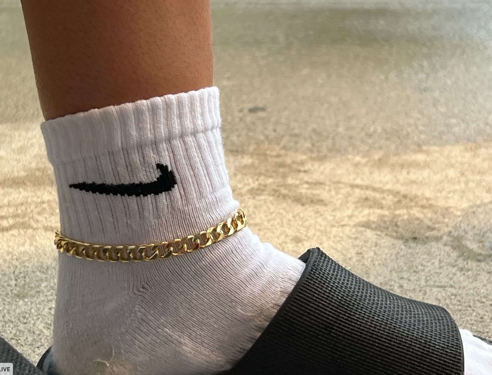 Close-up of reviewer wearing the white sock with slide sandal with gold ankle chain