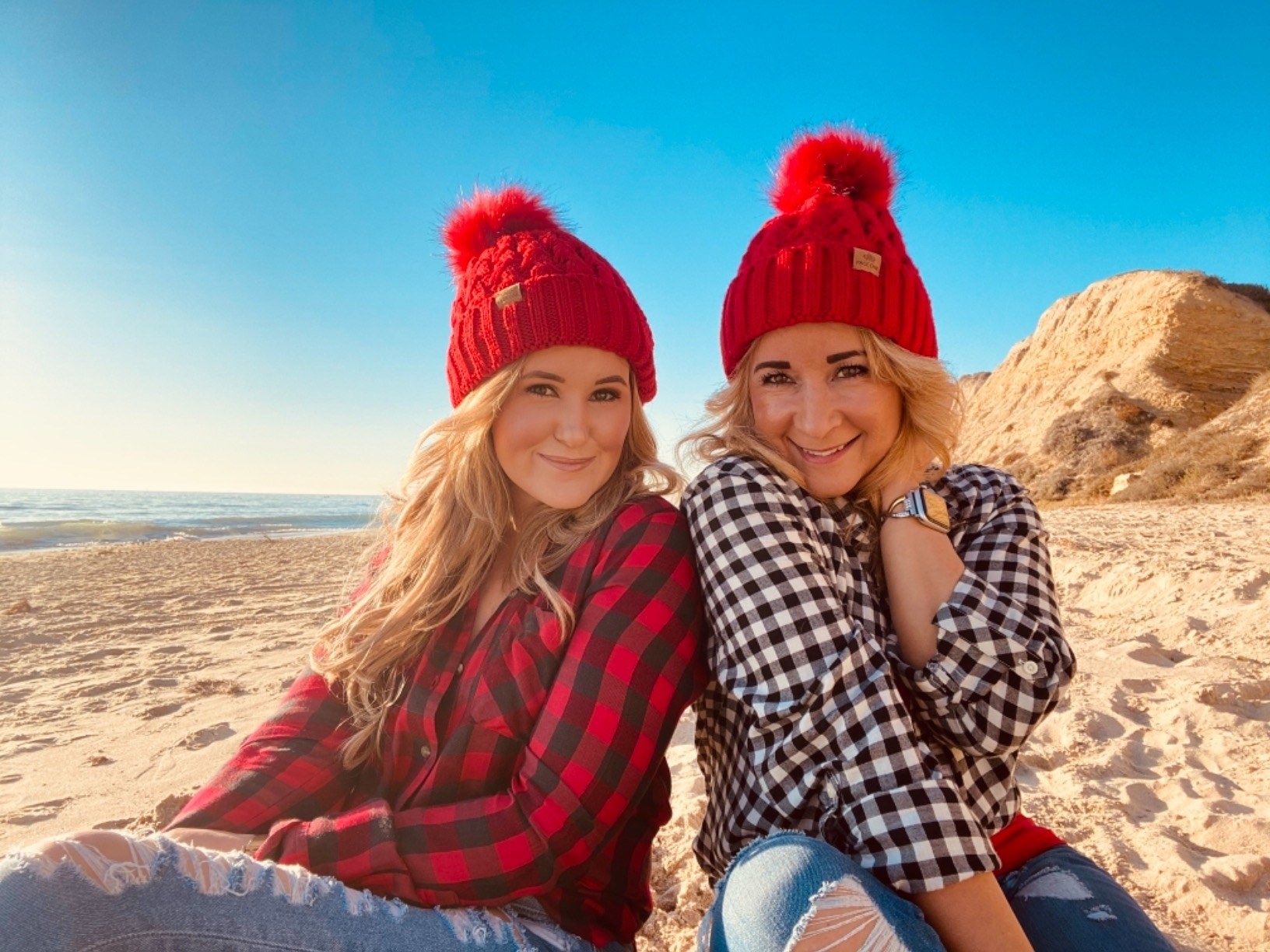 Two reviewers sitting on beach each wearing the red beanie