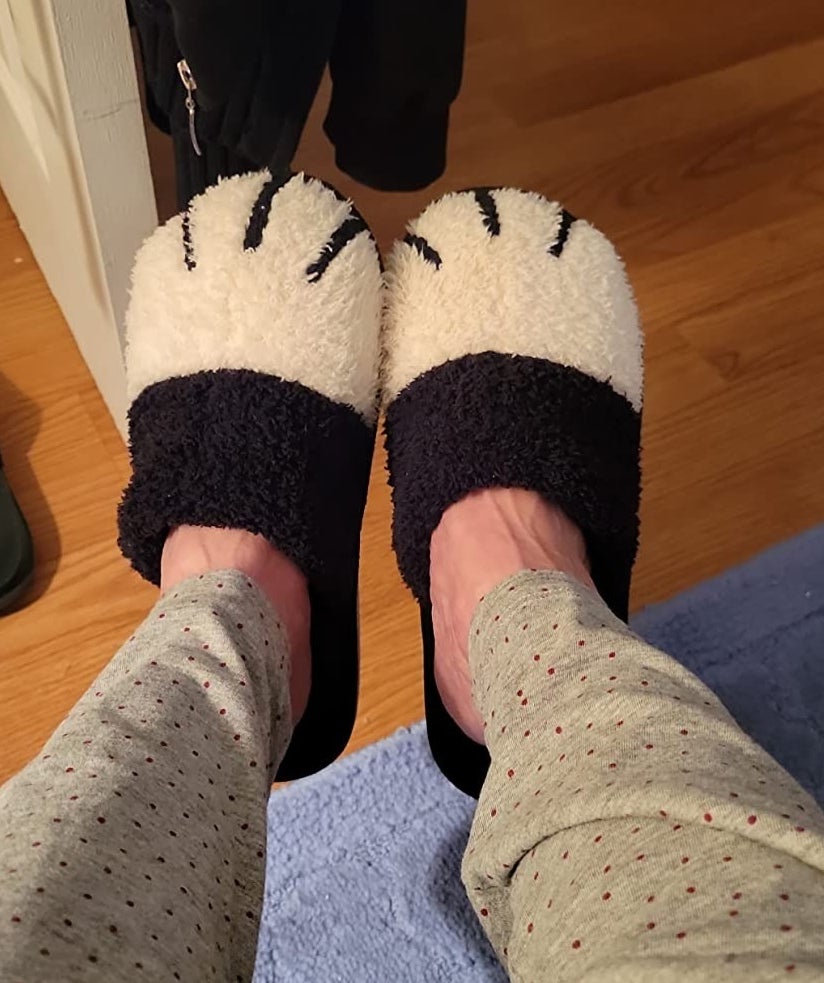 A reviewer in dotted gray pajama bottoms wearing the fuzzy white paw slippers with a black trim