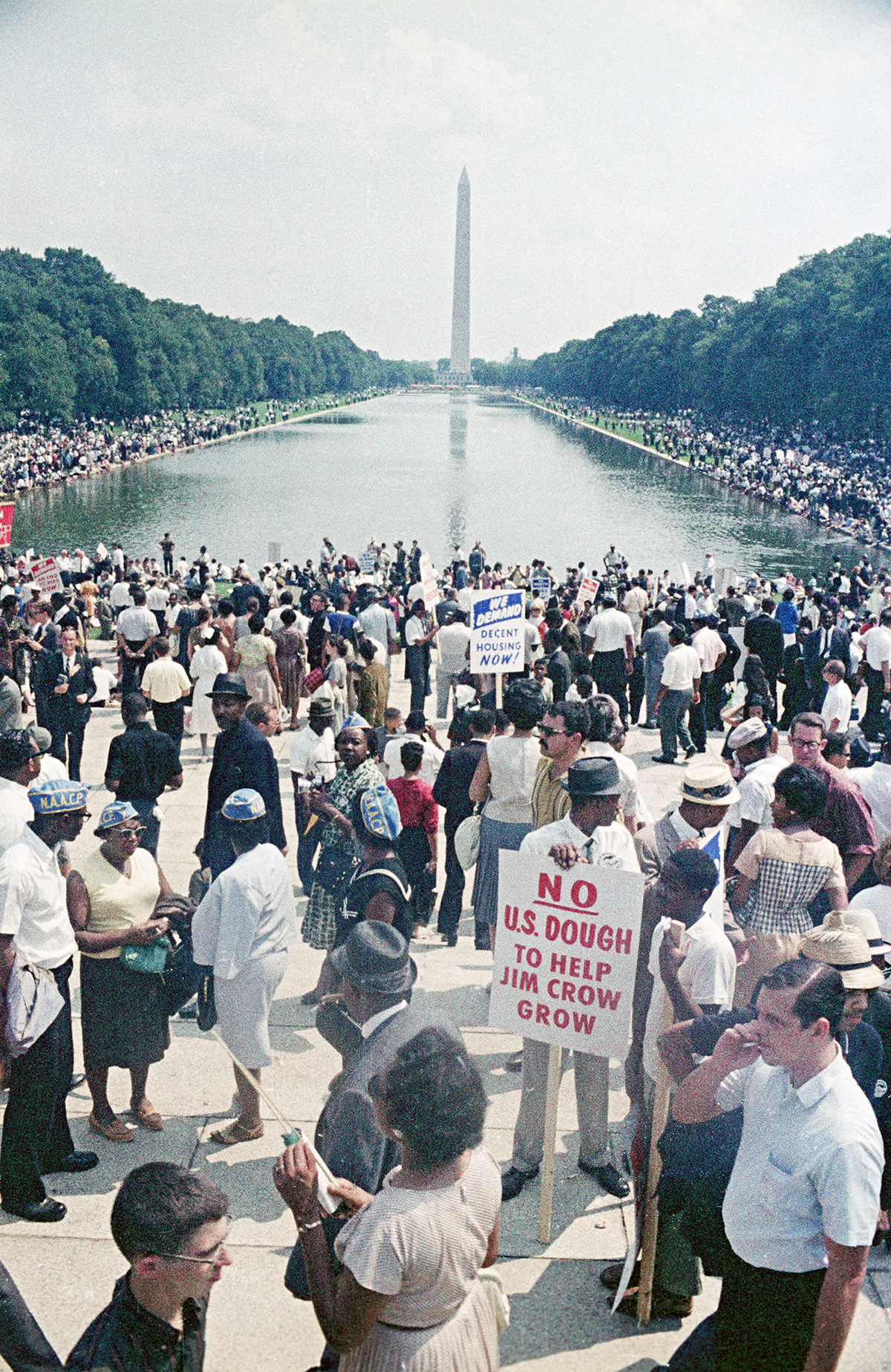 Attendees of the March on Washington hold signs with the Washington Monument in the background.