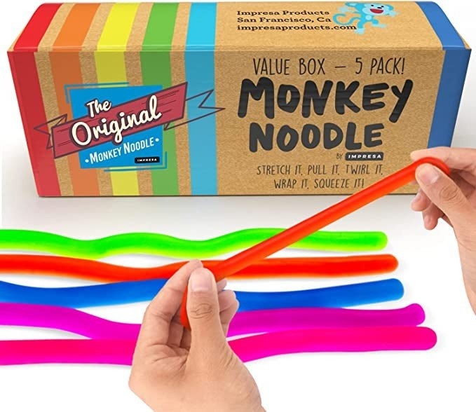 A model playing with a red monkey noodle in the forefront while the the rest of the noodles lay on a flat surface