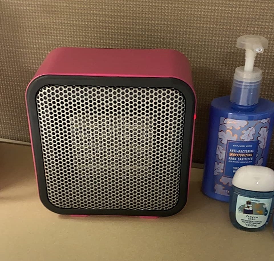 A reviewer picture of the pink ceramic heater with personal items to the right.